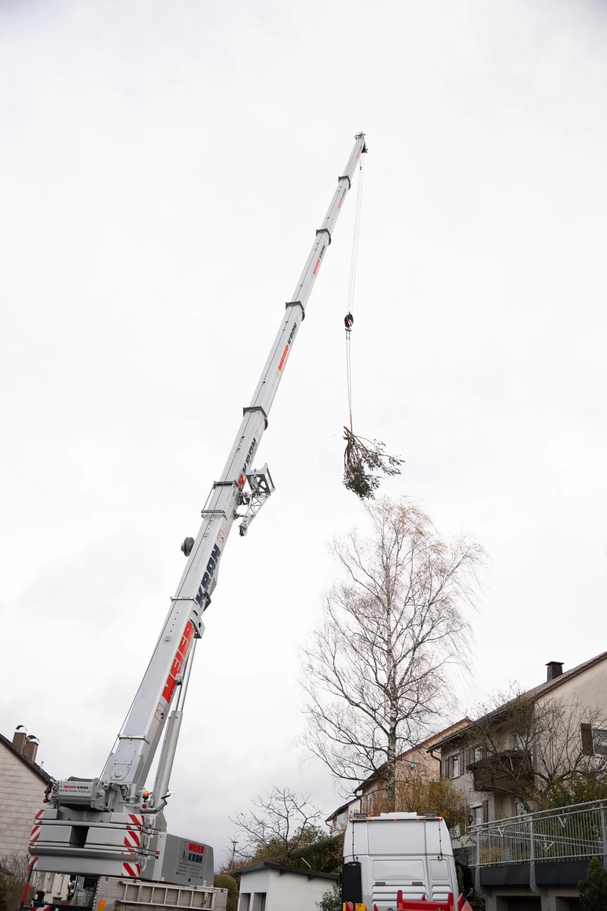 Teleskopkran hebt einen abgetrennten Baumwipfel im bebauten Stadtgebiet von Freyung an