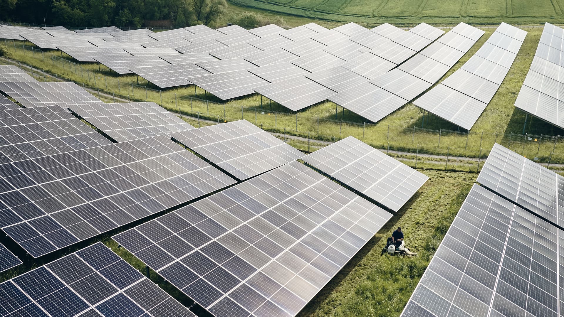 Luftaufnahme eines Solarparks: Aufsitzmäher mäht die Grünfläche zwischen den Modulreihen einer PV-Freiflächenanlage