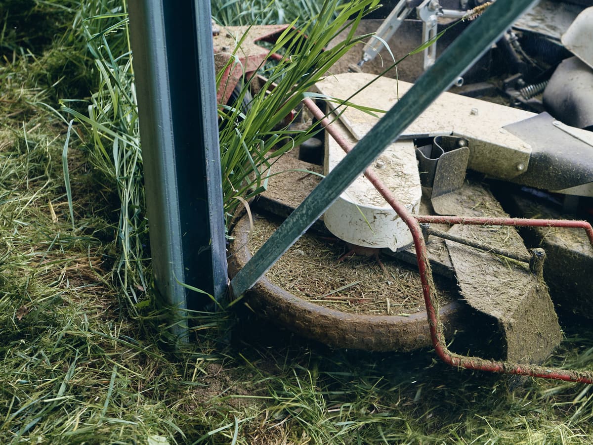 Mähwerk eines Aufsitzmähers schneidet den Bewuchs dicht an einem Modul-Montagepfosten im Solarpark